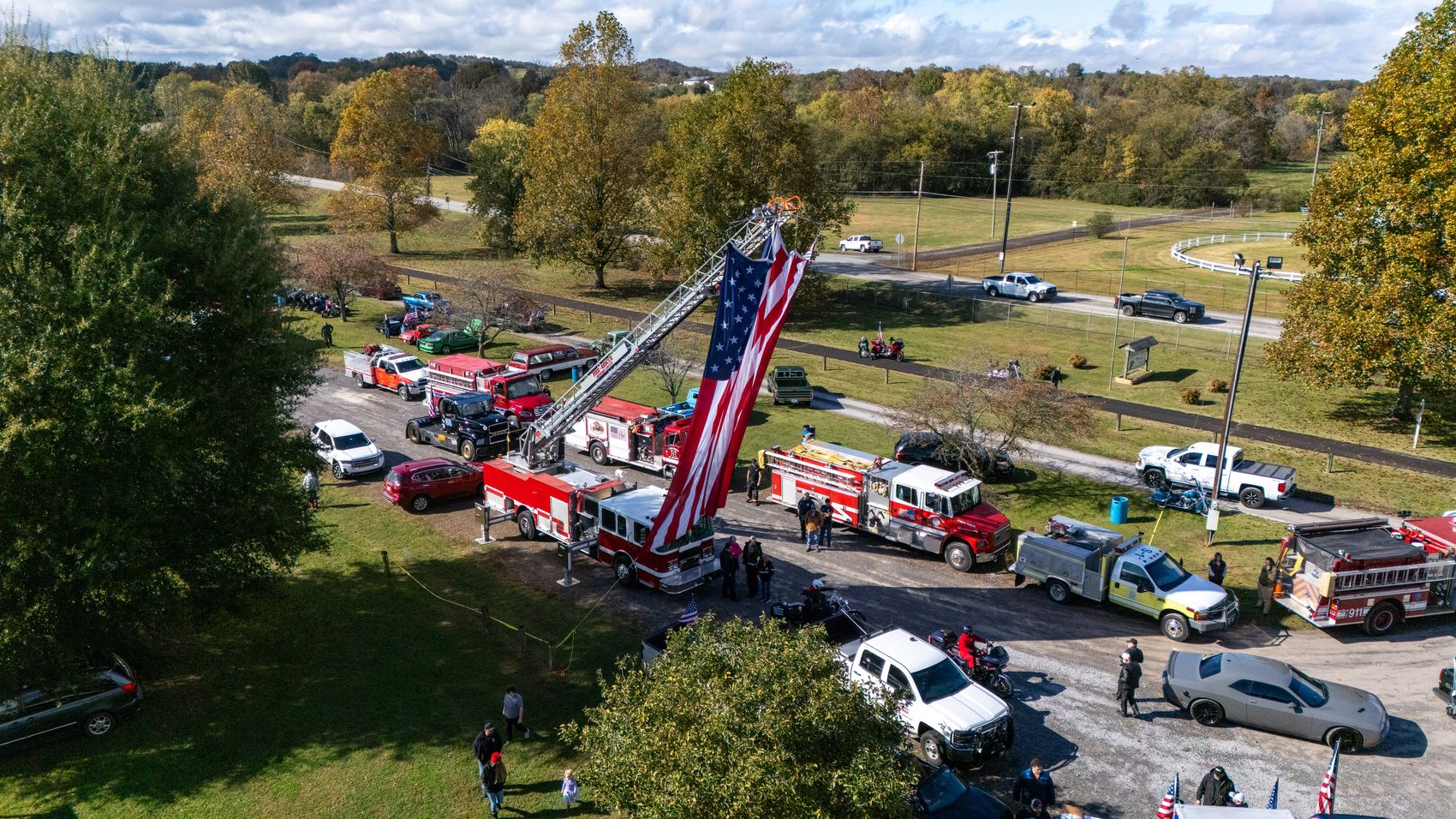 Aerial of a first-responder community event with fire apparatus and a large flag display
