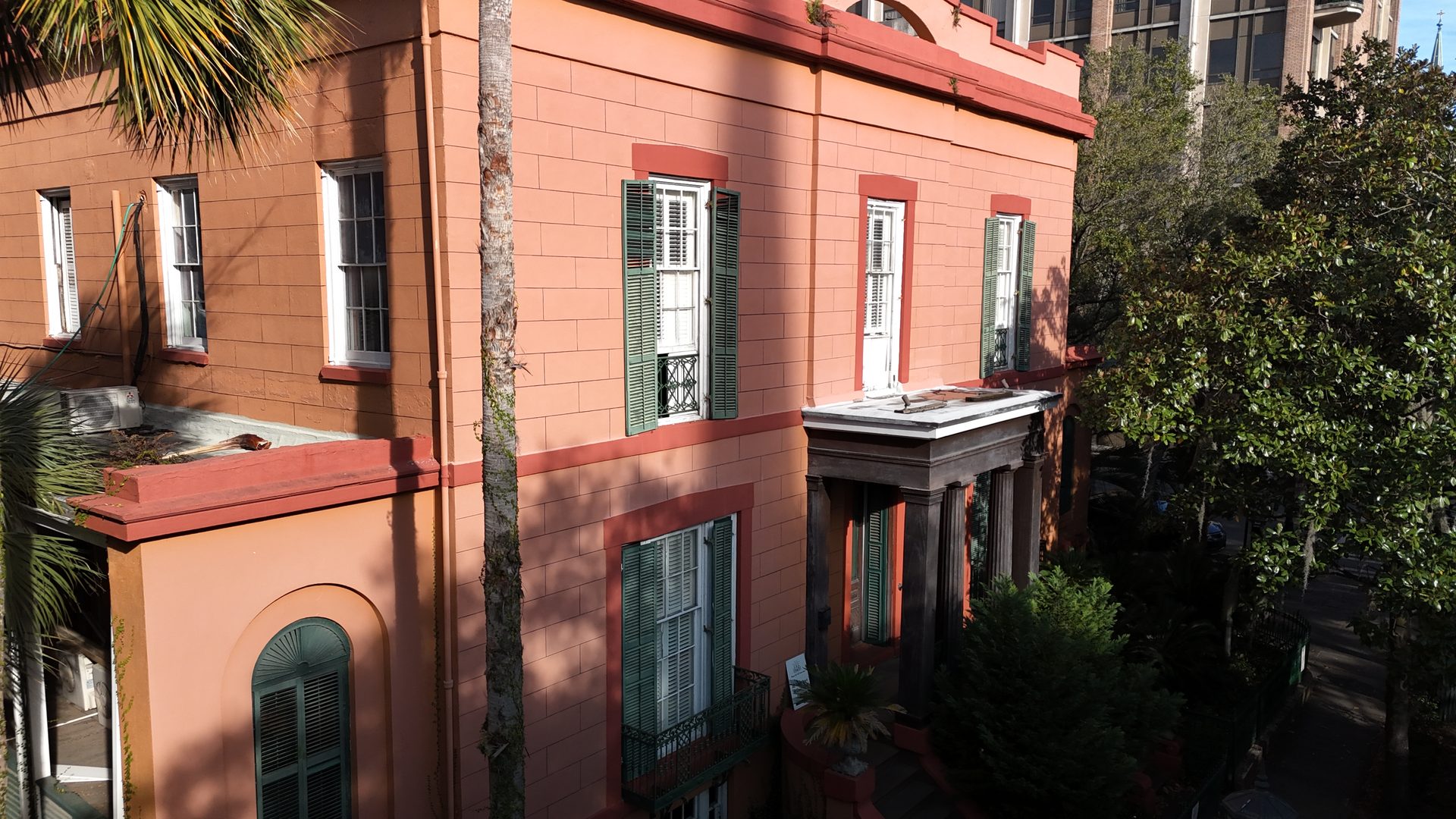 Oblique drone view of a historic building facade with green shutters and a columned entry, for elevation inspection
