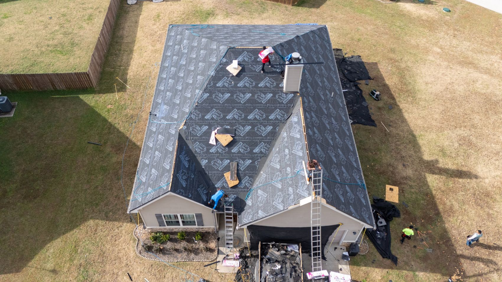 Aerial of a residential roof replacement in progress with crew and materials